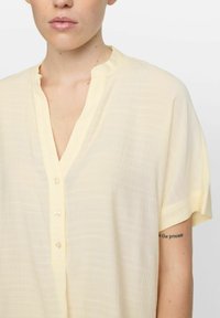 Lichtgele korte mouwen shirt van lichtgewicht, textuurstof met een halve knoopsluiting en een subtiele V-hals.