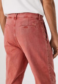 Pantaloni in denim rosso con una vestibilità rilassata, dotati di tasche posteriori e una texture sottile. La vita include un piccolo etichetta del marchio.