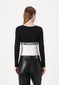 Long-sleeve top featuring a black upper section with a white lower section, branded waistband, and a round neckline. Worn with black leather pants.