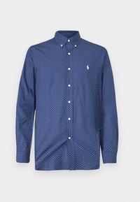 Mörkblå skjorta med knappar som har vita prickar, spetsig krage, långa ärmar och en liten logotyp på vänster bröst.