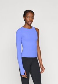 Μπλούζα με μακριά μανίκια, εφαρμοστή, σε ανοιχτό μωβ ύφασμα, με ασύμμετρο ντεκολτέ και ένα πλήρες μανίκι, συνδυασμένη με μαύρο κολάν.