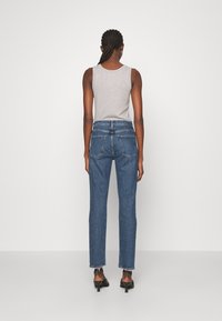 Siniset denimhousut suorahkolla lahkeensuu-leikkauksella, rispaantuneilla helmilla ja kahdella takataskulla. Yhdistetty harmaaseen hihattomaan toppiin.