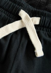 Fekete pamut rövidnadrág, rugalmas derékkal, krémszínű zsinórral, szövéssel. Sima anyag minta nélkül.