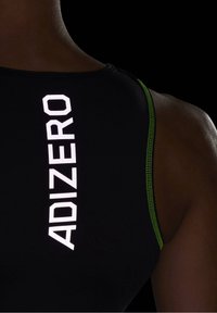 Gros plan sur le haut du dos d'une personne portant un haut de sport noir avec des surpiqures vertes et le mot "ADIZERO" imprimé verticalement en blanc.