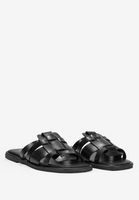 Sandales en cuir noir avec un design de brides tressées, bout ouvert, semelle plate et texture lisse. Style simple et minimaliste.