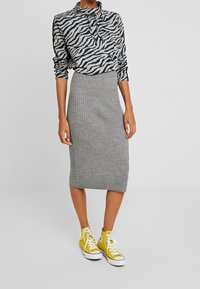 Jupe midi grise côtelée au design ajusté, associée à un pull zébré noir et blanc et des baskets montantes jaunes.
