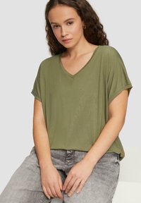 Olivengroene, korte mouwen V-hals t-shirt van zachte stof. Casual pasvorm met opgerolde mouwen, gecombineerd met lichtgrijze jeans.
