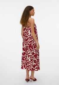 Robe maxi à motif rouge et crème avec de fines bretelles, au design fluide et à la coupe ample, assortie à des sandales à talons rouges.