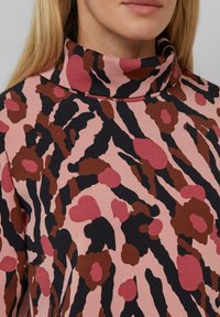 Rosa Stoffoberteil mit hohem Kragen, versehen mit einem auffälligen abstrakten Muster aus dunkelbraunen, schwarzen und gedämpften rosa Punkten und Streifen.