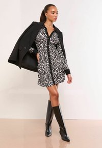 Rochie cămașă cu modele alb-negru, cu guler și închidere cu nasturi, completată cu un sacou negru și cizme lucioase negre până la genunchi.