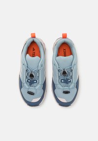 Scarpe da ginnastica azzurro chiaro con tomaia in rete, dettagli in blu navy, lacci elastici e soletta arancione, progettate per attività all'aperto.