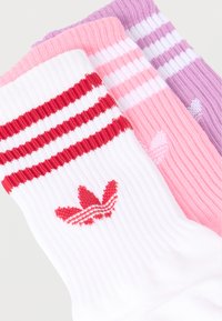 Three folded ribbed socks in white with red stripes and logo, pink with white stripes, and purple with white stripes on a white background.