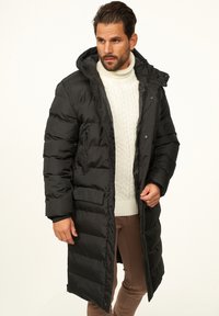 Schwarzer Steppmantel mit langem Design, Reißverschluss- und Knopfverschluss, zwei Vordertaschen und Kapuze. Warmes Material mit glatter Textur.