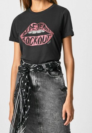 Kobieta w czarnej koszulce z różowym nadrukiem ust z napisem „Pepe Jeans Rockout” oraz w wyblakłej szarej dżinsowej spódnicy z paskiem w czarny wzór gwiazdek.