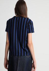 Czarny t-shirt z krótkim rękawem w pionowe niebieskie paski, wykonany z miękkiego materiału, charakteryzujący się luźnym krojem i zaokrąglonym dołem z tyłu.