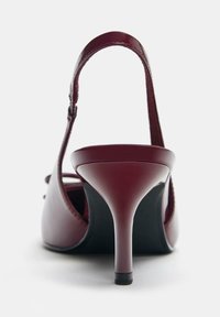 Bordo lakirani sandal z visokim peto, z zaponko, koničastim nosom in 7,5-centimetrsko špicasto peto. Črna gumijasta podplat z minimalnimi detajli.