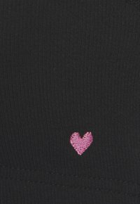 Small pink embroidered heart on black ribbed fabric with visible stitching at the bottom edge.