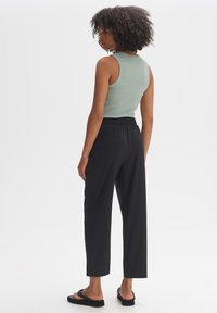 Mintgrünes, eng anliegendes Tanktop, kombiniert mit lockeren schwarzen Hosen; die Hosen haben einen elastischen Bund und einen taillierten Beinschnitt. Schwarze flache Sandalen.
