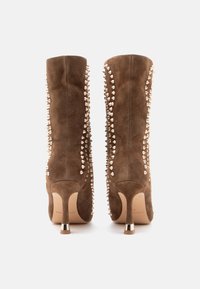 Botas de tobillo de ante marrón con acentos de picos metálicos a lo largo de los costados, con punta afilada y tacón de aguja con detalle metálico.