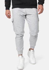Szare dresy z tapered legs i bocznymi kieszeniami cargo, wykonane z miękkiego materiału. Połączone z białymi trampkami z teksturowanymi detalami.
