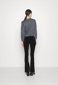 Pantalones de terciopelo negro con campana combinados con un suéter recortado de patrón azul y negro, que presenta diseños geométricos y rayas texturizadas.