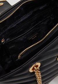 Mustat tilkkuhatut käsilaukku kultaisilla yksityiskohdilla, jossa on vuorattu sisustus useilla taskuilla ja vetoketjullinen suljinta.
