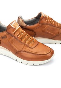 Zapatillas de cuero marrón con un acabado suave, con cordones beige y una suela de goma blanca en contraste. Logo notable en la lengüeta.