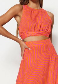 Ensemble deux pièces à motifs roses et orange comprenant un haut court sans manches et une jupe évasée à rayures ondulées, confectionné dans un tissu léger.