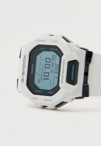Casio G-Shock Digitaluhr mit weißem Resinarmband, schwarzen Akzenten und einem rechteckigen Gehäuse mit blauem Display und verschiedenen Funktionstasten.