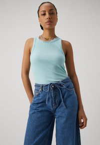 Lys blå ribbet tanktop med et mønstrete halsutringning, matchet med høy midje lys blå denim vid bukser og knyttet beltedetalj.