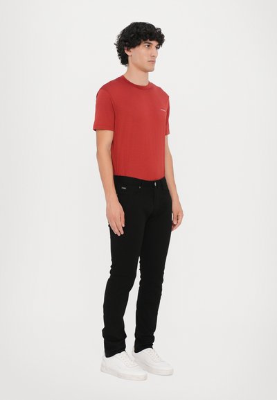 Rotes Kurzarm-T-Shirt, schwarze Slim-Fit-Jeans und weiße Sneakers. Das T-Shirt hat ein dezentes Logo auf der Brust. Einfaches Design, lässige Kleidung.