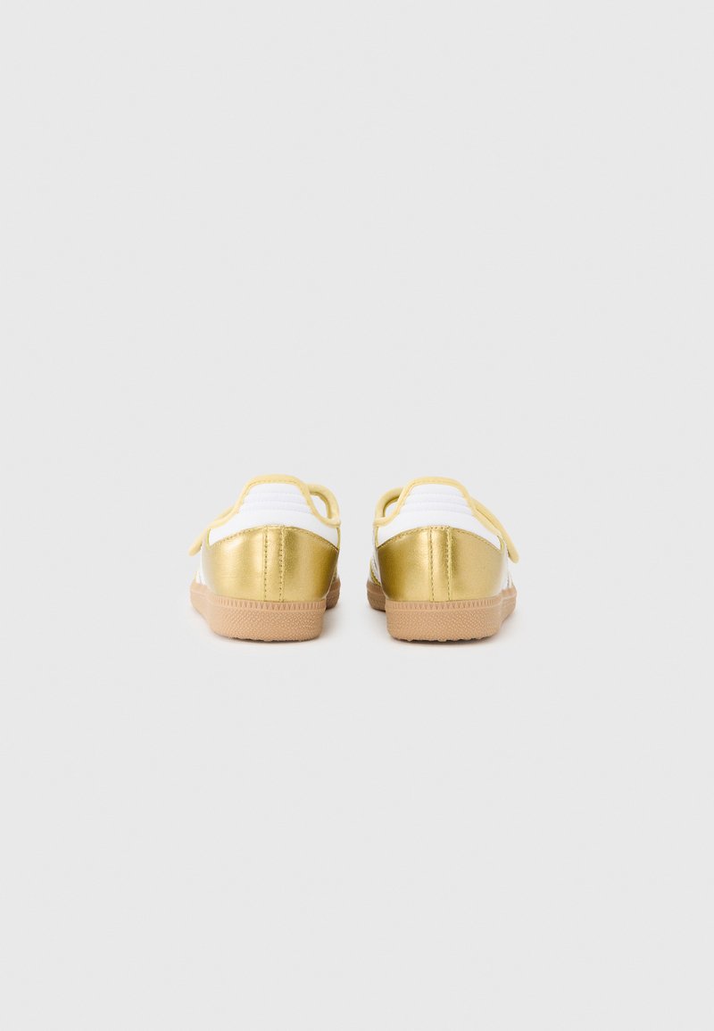 Gold and white sneakers with a textured finish, featuring a smooth gold heel, white textile upper, and rubber sole.