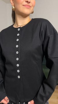 Mustast materjalist pika varrukaga pluus ümarate kaelusega, millel on ees kuus halli nööpi ja tekstuurse viimistlusega.