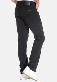 Jeans en denim noir avec une coupe droite, des coutures visibles et deux poches arrière. Comprend une étiquette en cuir au niveau de la taille.