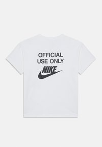 Biely tričko s krátkym rukávom so čiernym nápisom "LEN NA OFICIÁLNE POUŽITIE" a logom Nike na zadnej strane, vyrobené z bavlny.