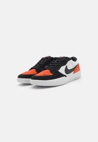 Tênis pretos e laranja com materiais de camurça e tecido; sola branca; logotipo Nike preto; detalhe de biqueira perfurada; design com atacadores.