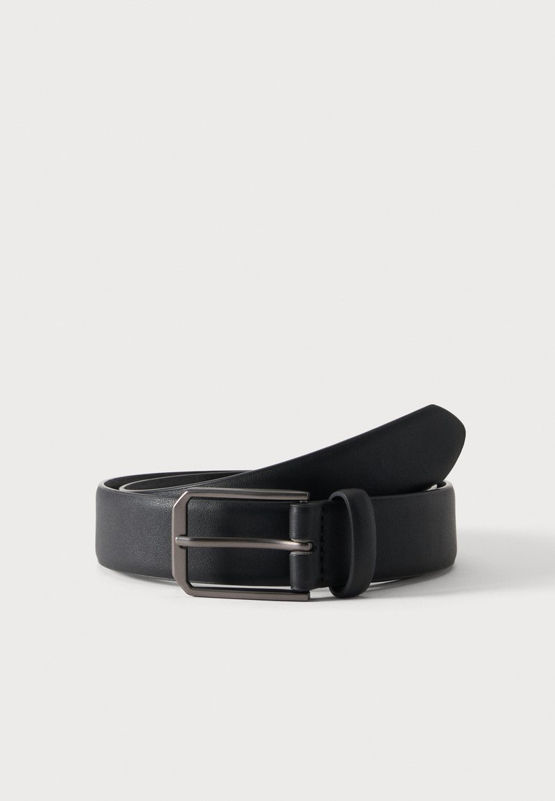 Ceinture en cuir noir roulée avec une boucle métallique argentée rectangulaire sur un fond clair uni.