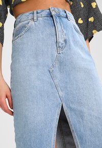 Light blue denim skirt featuring a front slit, a high waist, and traditional belt loops. The fabric has a subtle texture and classic design.