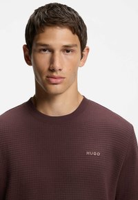 Sweatshirt texturé à manches longues de couleur bordeaux avec un col rond et un logo "HUGO" subtil brodé sur la poitrine.