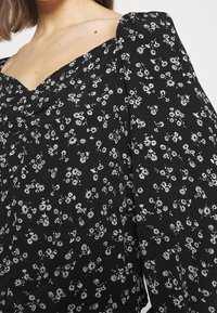 Blusa nera floreale con vestibilità morbida, ampie maniche volanti e piccoli fiori bianchi su tutta la stoffa, caratterizzata da un design a scollatura a V.