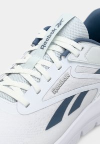 Valkoiset urheilukengät, joissa on vaaleansinisiä yksityiskohtia, verkkopäällinen, pyöreät nauhat ja Reebok-logo kielekkeellä. Tekstuuroitu pinta, jossa on tummansinisiä muotoilu elementtejä.