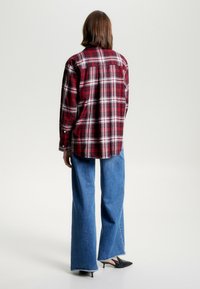 Rød- og hvidternet flannelskjorte med lange ærmer og afrundet kant, kombineret med vidbenede blå denimbukser og sorte hæle.