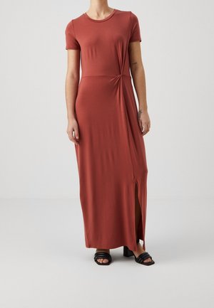 Maxi-jurk in roest, korte mouwen, zachte stretchy stof. Heeft een zijknoopdetail en een split tot aan de dij. Gepaard met zwarte hoge hakken sandalen.