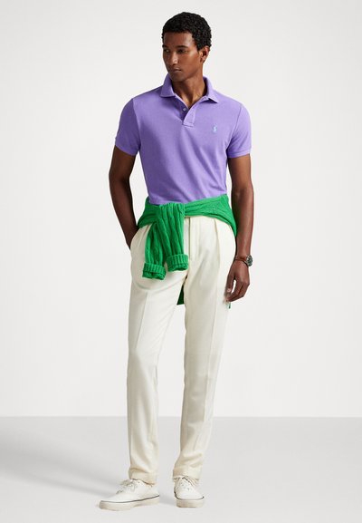 Vijolična polo majica s kratkimi rokavi, bele hlače, zelena jopica zavezana okoli pasu in bele superge. Preprosta zasnova s kontrastnimi barvami.