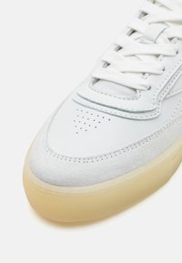 Sneaker bianca in pelle con dettagli in morbido suede, punta tonda, lacci bianchi piatti e suola in gomma traslucida con finitura testurizzata.
