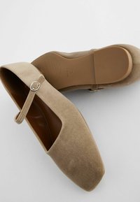 Beez suede kingad ruudukujulise nina, pahkluu rihma ja hõbeda pandlaga. Lame tald peene tekstuuriga. Ülemine vaade näitab puhtaid jooni ja minimalistlikku disaini.