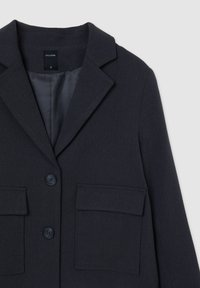 Blazer bleu marine avec revers en pointe, deux poches avant et fermeture à deux boutons. Tissu texturé avec une doublure intérieure lisse.