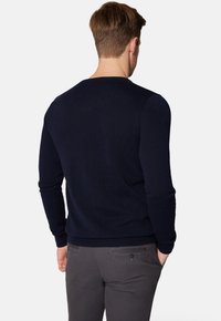 Granatowy sweter dzianinowy z okrągłym dekoltem i ściągaczami, noszony przez osobę odwróconą tyłem. Charakteryzuje się gładką fakturą i dopasowanym krojem.