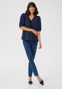 Top azul marino con mangas cortas abullonadas y escote en V, combinado con vaqueros ajustados azul y bailarinas negras de punta. Tejido texturizado con rayas sutiles.