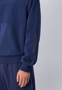 Felpa blu navy realizzata in tessuto morbido, con un pannello orizzontale in contrasto e dettagli del logo sulla manica.
